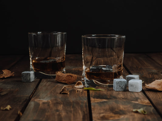 Zwei Gläser mit Whiskey gefüllt, Whiskeysteine daneben