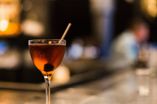 Manhattan Cocktail vor unscharfem Hintergrund mit Kirsche garniert | Old Soggy Spiced Bourbon