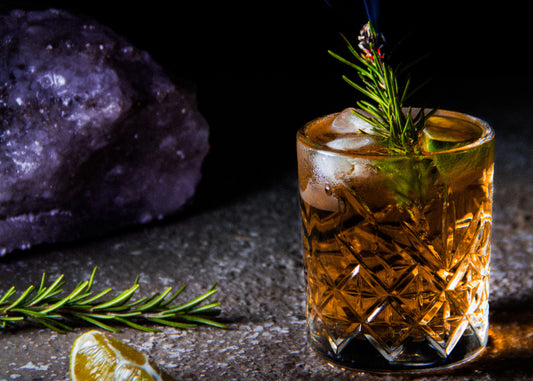 Cocktail vor schwarzem Hintergrund mit Rosmarin und Zitrusfrüchten
